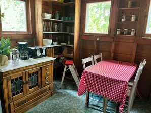 Een kleine keuken met houten kastjes, een koffiezetapparaat en een tafel met een rode geruit tafelkleed.