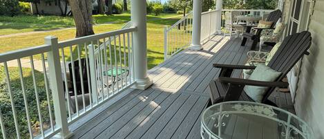 A covered porch with a wooden deck, white railings, and outdoor furniture including chairs and a table.