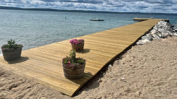 A wooden pier extending into calm water, with potted plants on either end. - Charming 5-bedroom Roaring Brook cottage in Harbor Springs with beach access. (Harbor Springs)