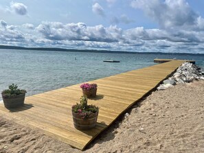 Une jetée en bois s’avançant dans une étendue d’eau calme, avec des plantes en pot à chaque extrémité.