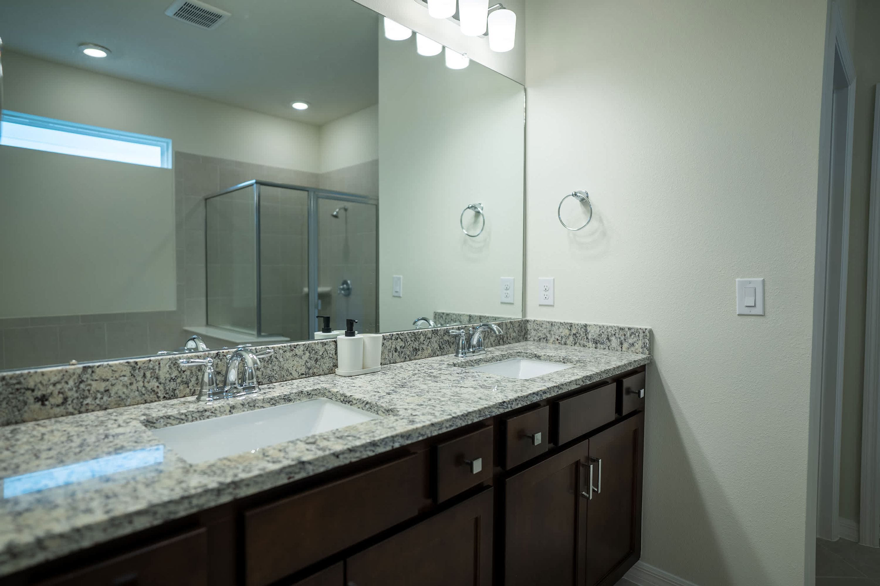 A modern bathroom with a granite countertop, dual sinks, and a large mirror.
