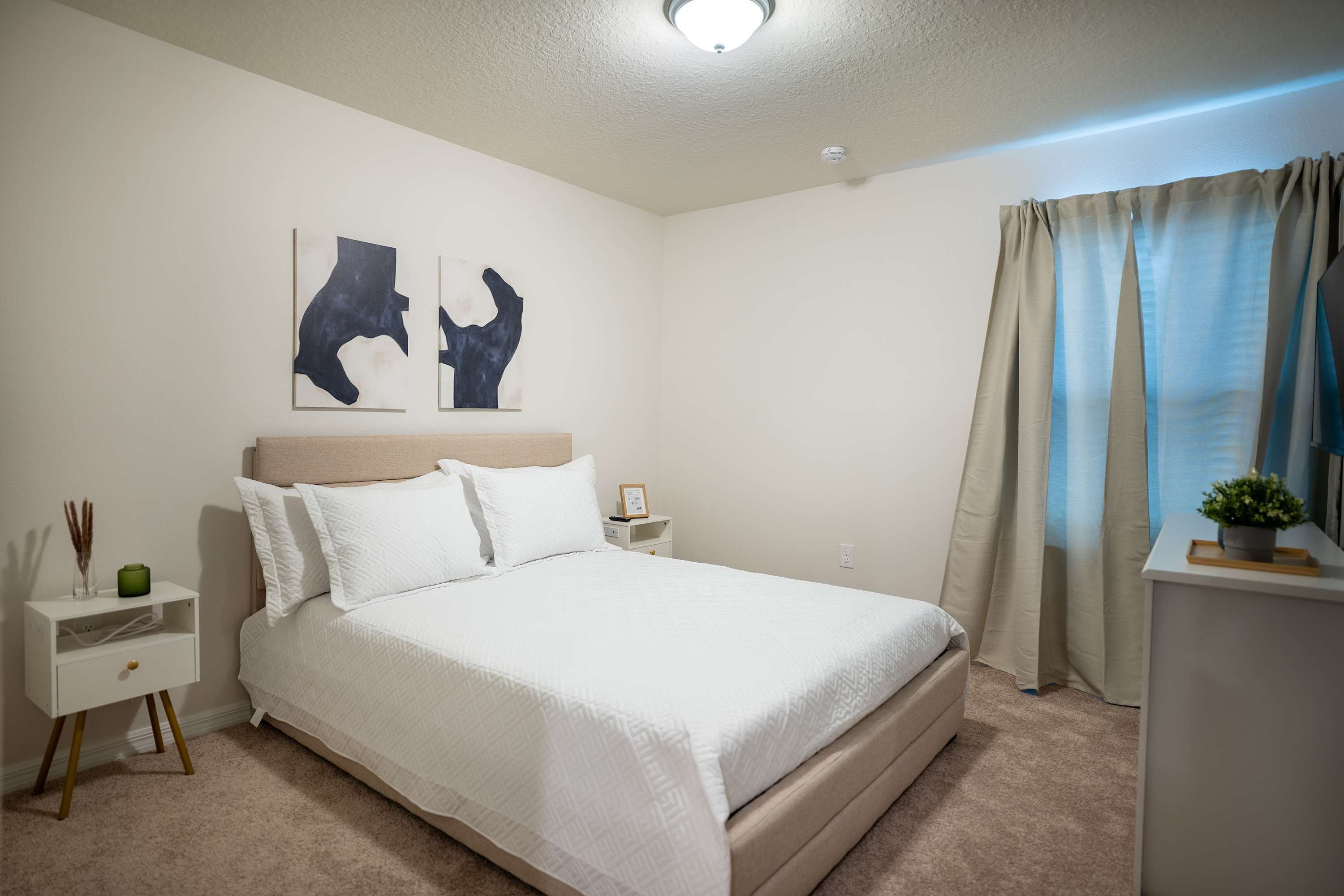 Un dormitorio ordenado con cama, mesitas de noche y cuadros en la pared.