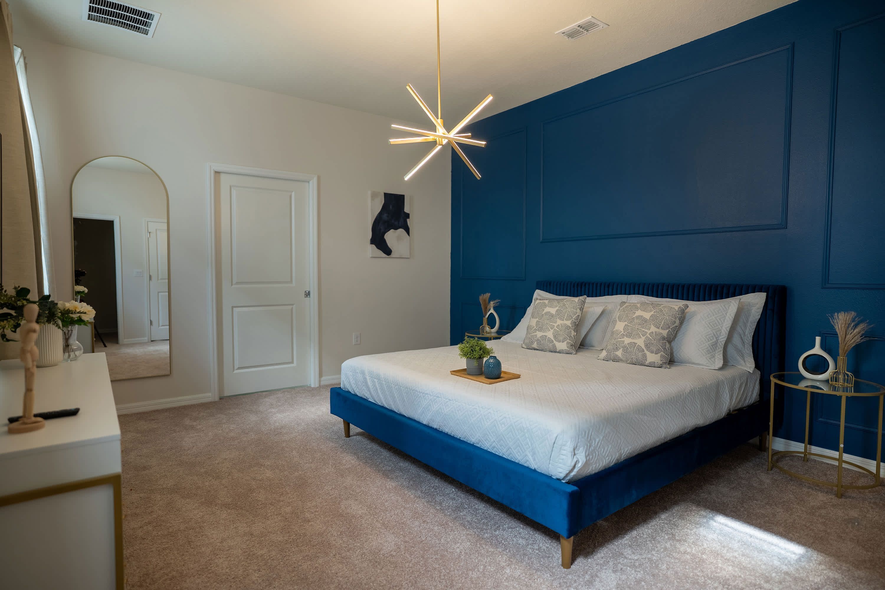 A bedroom with a bed, a bedside table, a mirror, and a wall-mounted artwork.