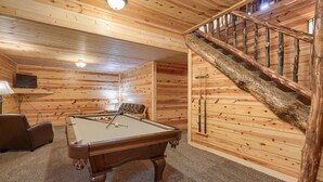 Une pièce aux murs lambrissés, avec une table de billard, un canapé et un escalier.