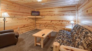 L’intérieur d’un chalet chaleureux, avec des murs en bois, un canapé, une table basse et un téléviseur fixé au mur.
