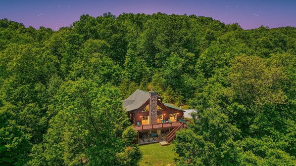 A log cabin with a stone chimney, surrounded by dense forest. - Waccabuck | 17.5 Private Acres, Pool, Hot Tub (Logan)