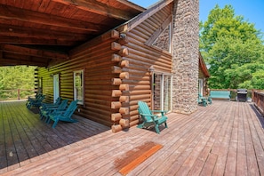 A log cabin with a wooden deck, outdoor seating, and a stone chimney.