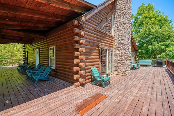 A log cabin with a wooden deck, outdoor seating, and a stone chimney.