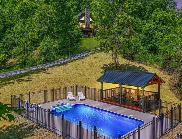A swimming pool with a fenced deck, lounge chairs, and a gazebo.