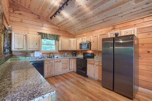 A kitchen with wooden cabinets, granite countertops, stainless steel appliances, and a window with a view.