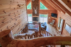 A wooden cabin interior with a stone fireplace, a mounted television, and a wooden staircase.