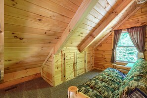 A cozy attic bedroom with wooden walls, a sloped ceiling, a bed with patterned bedding, and a window with curtains. - Waccabuck | 17.5 Private Acres, Pool, Hot Tub (Logan)