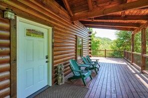 A log cabin with a porch, a door with a sign, and two green chairs.