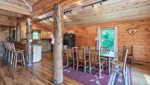 Un intérieur de cabine spacieux avec des planchers en bois, un coin repas avec des chaises en bois, une cuisine avec des meubles en bois et une grande fenêtre offrant une vue sur la verdure.