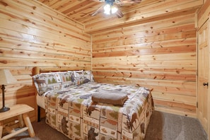 A wooden-paneled bedroom with a bed, a nightstand, and a ceiling fan.
