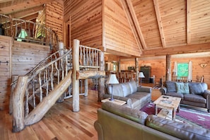 A log cabin interior with a wooden staircase, leather sofas, and a dining area.