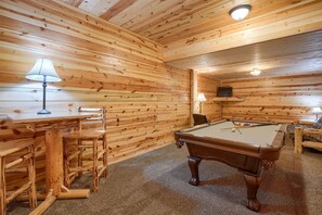 A wooden-paneled room with a pool table, chairs, and lamps.