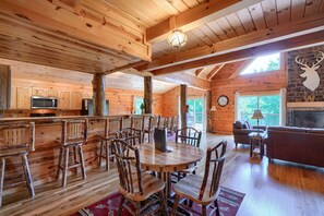 A wooden cabin interior with a dining area, kitchen, and living room. - Waccabuck | 17.5 Private Acres, Pool, Hot Tub (Logan)