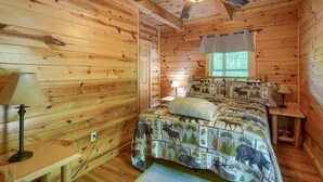 Une pièce de type cabane en bois, avec un lit, deux lampes, un ventilateur de plafond et une fenêtre avec des rideaux.