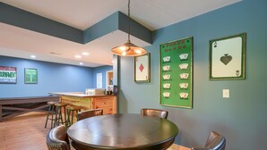 A dining area with a round table and chairs, a hanging light fixture, and poker hand posters on the wall. - Sandstone Valley Estate | Hocking, Indoor Pool (Logan)
