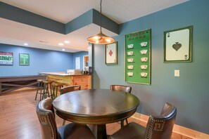 A dining area with a round table and chairs, a hanging light fixture, and poker hand posters on the wall.