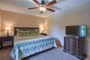 Une chambre à coucher comprenant un lit, deux tables de chevet avec des lampes, un ventilateur de plafond, une commode et un téléviseur.