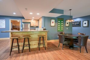 A kitchen with wooden cabinets, a bar area with stools, a dining table with chairs, and a ceiling light fixture.