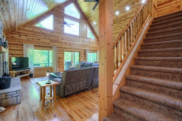 L’intérieur d’un chalet en bois, avec une cheminée, un canapé, un téléviseur et un escalier.