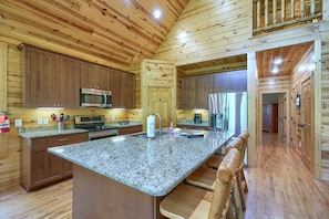 A kitchen with wooden paneling, granite countertops, stainless steel appliances, and a bar area with stools. - Sandstone Valley Estate | Hocking, Indoor Pool (Logan)