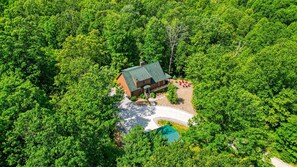 An aerial view of a house surrounded by dense green forest.