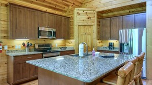 A kitchen with wooden cabinets, granite countertops, stainless steel appliances, and a wooden bench. - Sandstone Valley Estate | Hocking, Indoor Pool (Logan)