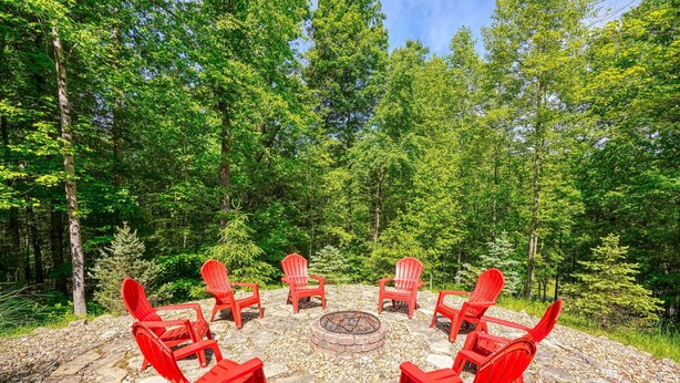 A circular seating arrangement with chairs around a central fire pit, set on a stone surface in a forested area. - Sandstone Valley Estate | Hocking, Indoor Pool (Logan)
