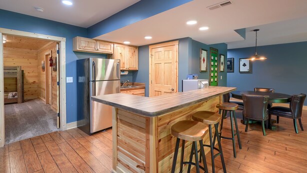 A modern kitchen with wooden cabinets, a stainless steel refrigerator, and a bar area with stools. - Sandstone Valley Estate | Hocking, Indoor Pool (Logan)