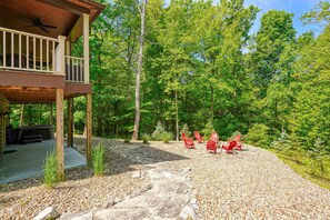 A wooden deck with a ceiling fan, a stone pathway, and red Adirondack chairs in a forested area. - Sandstone Valley Estate | Hocking, Indoor Pool (Logan)