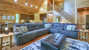 A spacious living room with a large sectional sofa, a leather ottoman, and a staircase leading to an upper level. - Sandstone Valley Estate | Hocking, Indoor Pool (Logan)