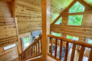 Ein Holzinnenraum einer Hütte mit Treppe, Holzwänden und mehreren Fenstern.
