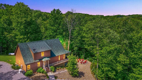 A cabin with a green roof, surrounded by dense forest.