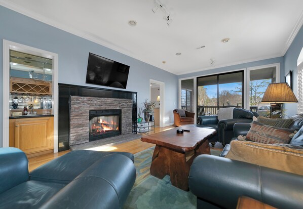 A spacious living room with a fireplace, leather sofas, a coffee table, and a television mounted above the fireplace.