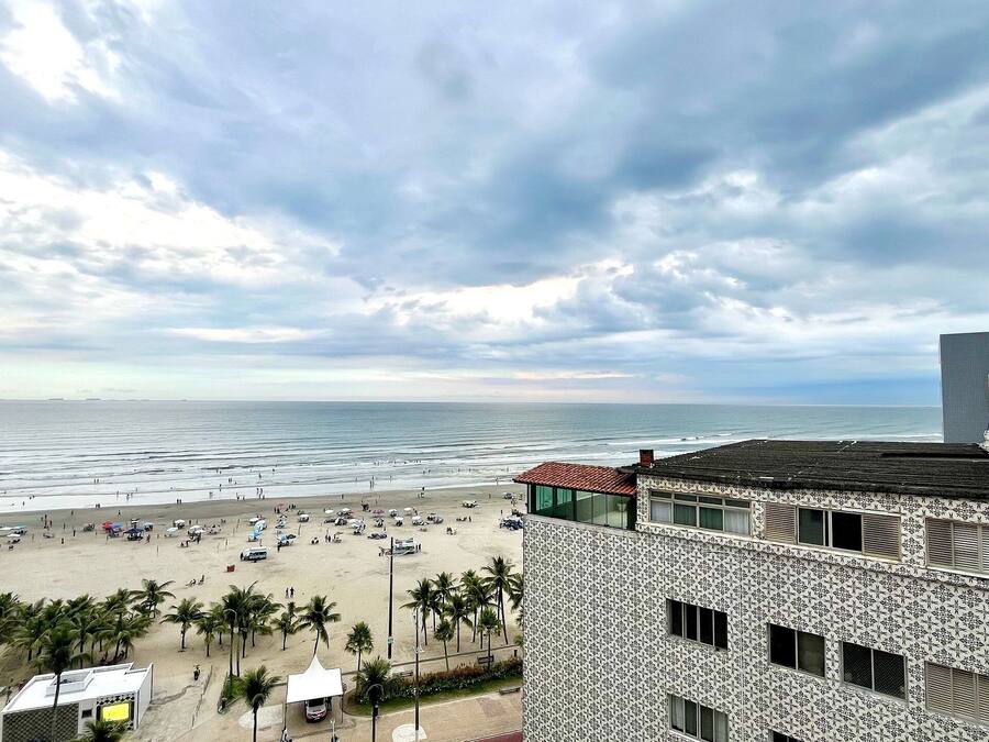 Vista de la playa con un edificio de paredes exteriores con diseños, palmeras y sombrillas.