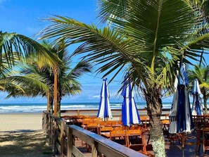 Zona relax in spiaggia con sedie di legno e ombrelloni blu e bianchi, vista sull'oceano.