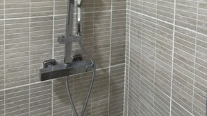 A shower with a handheld showerhead and a fixed overhead showerhead, mounted on a wall with a tiled pattern.