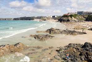 A coastal beach with rocky areas, a sandy shore, and buildings in the background. - 7 Whitehouse invites six guests to enjoy a slice of Cornish paradise (Newquay)