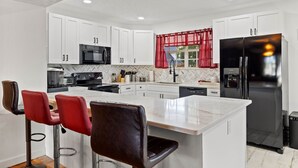 Una cocina moderna con armarios blancos, un refrigerador negro y una isla central con taburetes de bar.