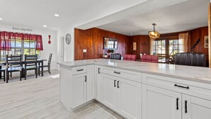 Una cocina moderna con armarios blancos, encimera de mármol y zona de comedor con sillas de madera y un sofá rojo.