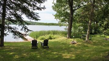 Un cadre idyllique au bord du lac, avec deux fauteuils Adirondack, une table de pique-nique et une pelouse.