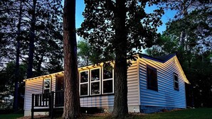 A small cabin with a porch, surrounded by trees.