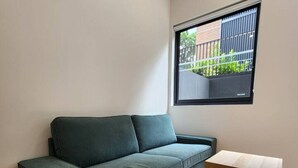 A room with a dark green sofa, a wooden table, and a window with a view of a balcony.