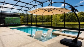 An indoor swimming pool with a large screen, lounge chairs, and a view of a lake.