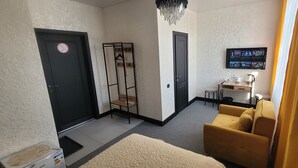 Une pièce comprenant un canapé, un bureau avec un ordinateur, un téléviseur fixé au mur et une porte sur laquelle est apposé un panneau « interdiction de fumer ».