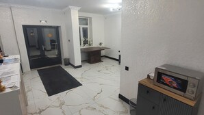 Une chambre d’hôtel avec un sol en marbre, un bureau avec un ordinateur, un petit placard et une porte donnant sur une autre pièce.